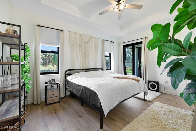 bedroom featuring access to outside, a tray ceiling, wood finished floors, and baseboards