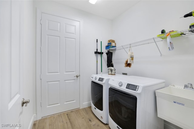 clothes washing area with light wood finished floors, a sink, washer and dryer, laundry area, and baseboards