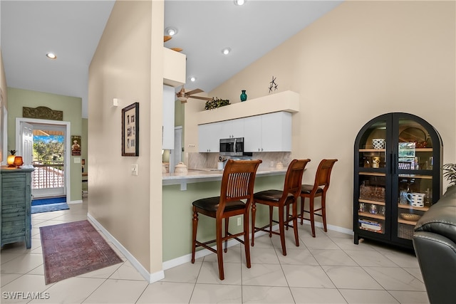 kitchen with high vaulted ceiling, white cabinets, tasteful backsplash, kitchen peninsula, and a breakfast bar area