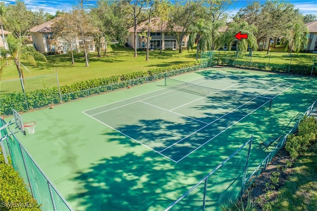 view of tennis court with basketball hoop and a yard