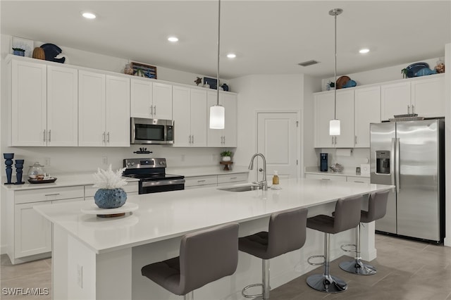 kitchen with an island with sink, hanging light fixtures, and appliances with stainless steel finishes