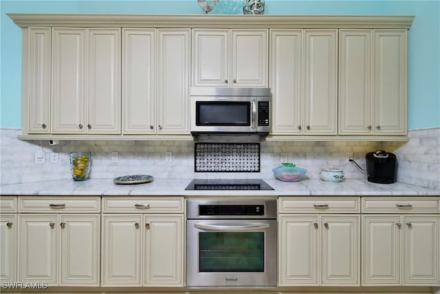 kitchen with backsplash, light stone countertops, stainless steel appliances, and cream cabinets