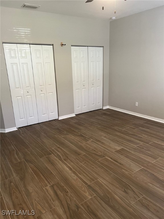 unfurnished bedroom featuring ceiling fan, dark wood-type flooring, and multiple closets