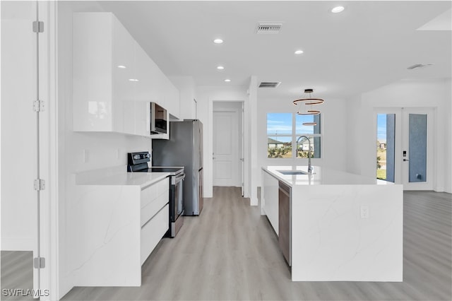 kitchen featuring white cabinetry, sink, stainless steel appliances, an island with sink, and light hardwood / wood-style floors