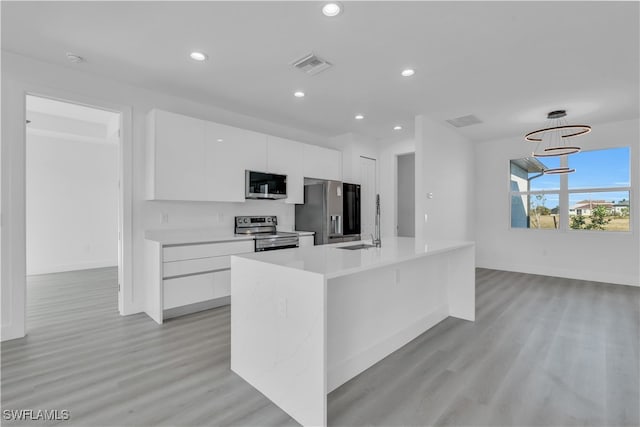 kitchen featuring light wood-type flooring, stainless steel appliances, white cabinetry, and a kitchen island with sink