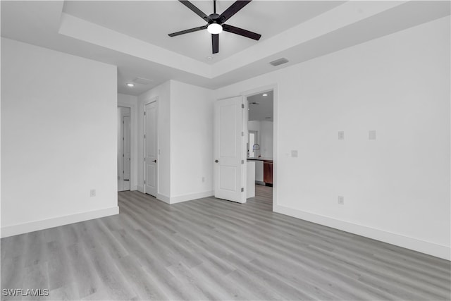 unfurnished bedroom with a tray ceiling, ceiling fan, and light wood-type flooring