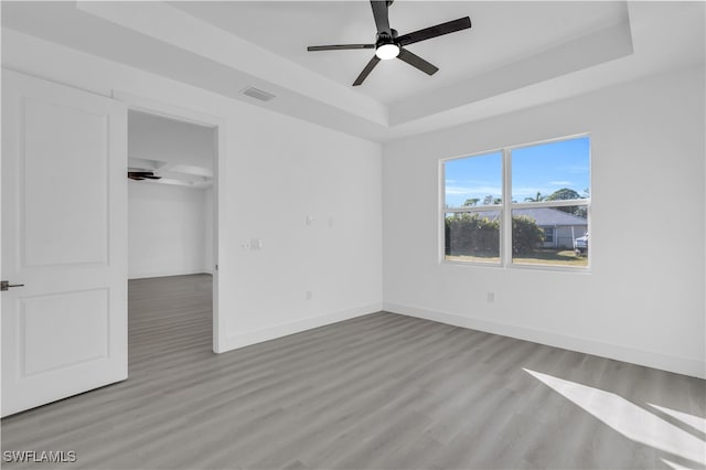 unfurnished bedroom with ceiling fan, a walk in closet, light wood-type flooring, and a tray ceiling