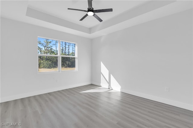 unfurnished room with a raised ceiling, ceiling fan, and light hardwood / wood-style floors