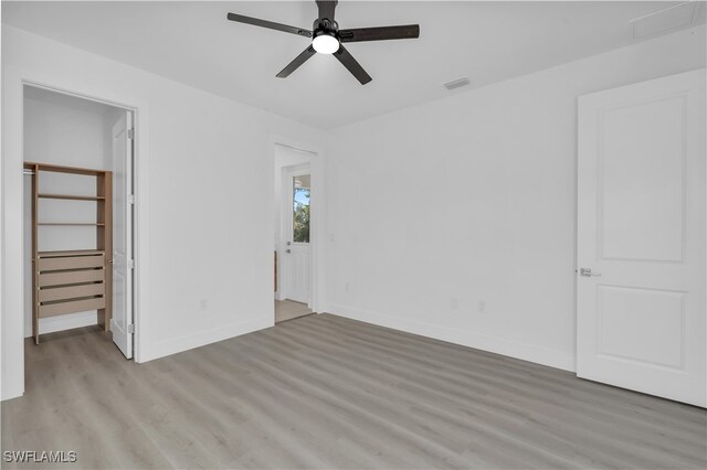 unfurnished bedroom with a walk in closet, light wood-type flooring, a closet, and ceiling fan