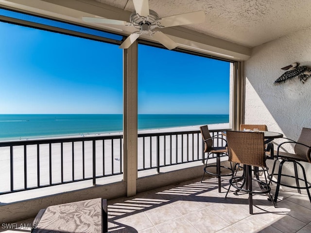 balcony with a view of the beach, a water view, and ceiling fan