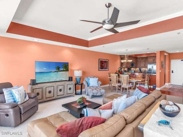 carpeted living room featuring ceiling fan with notable chandelier, ornamental molding, and a tray ceiling