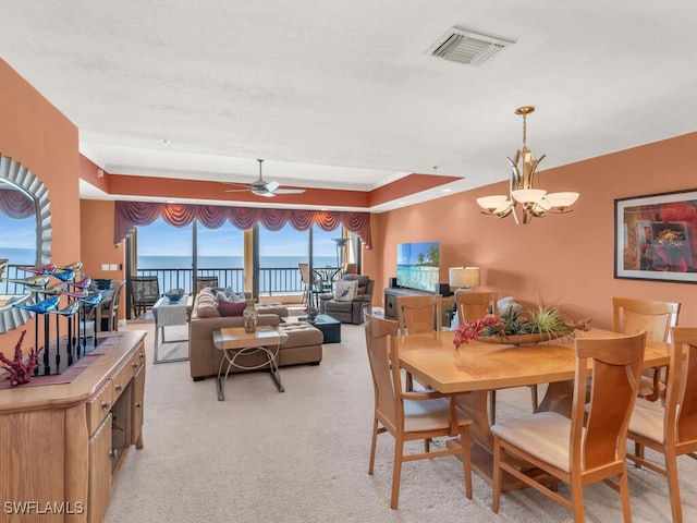 carpeted dining area with a tray ceiling, a water view, and ceiling fan with notable chandelier