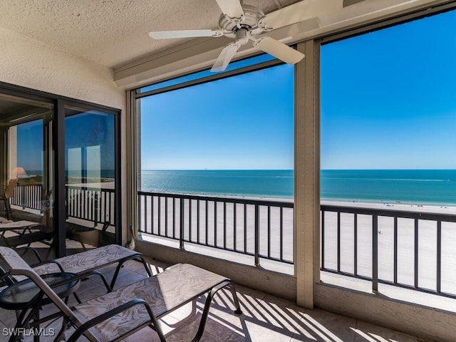 sunroom / solarium featuring a view of the beach, a water view, and ceiling fan