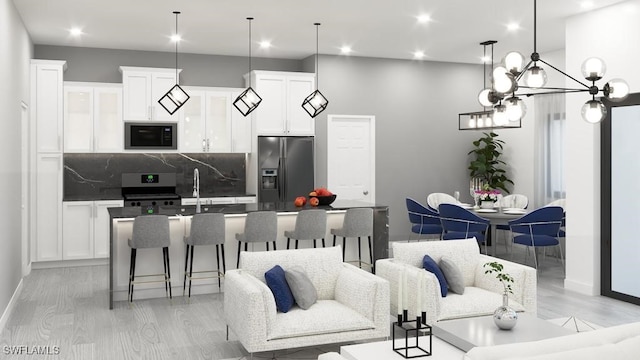 kitchen with hanging light fixtures, appliances with stainless steel finishes, white cabinetry, and a kitchen island with sink