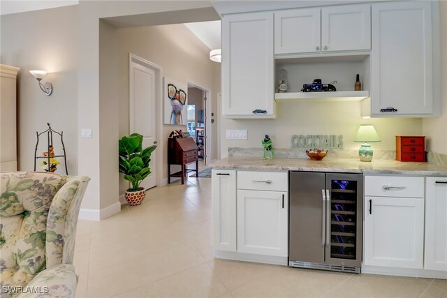 kitchen featuring wine cooler, light stone counters, white cabinets, and light tile patterned floors