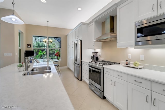 kitchen featuring sink, hanging light fixtures, stainless steel appliances, wall chimney range hood, and white cabinets