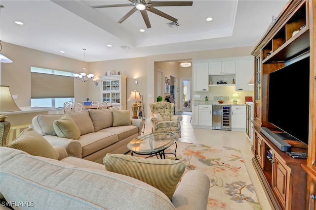 tiled living room featuring a raised ceiling, wine cooler, and ceiling fan with notable chandelier