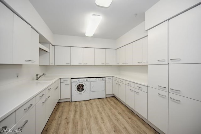 laundry room featuring light hardwood / wood-style floors, cabinets, sink, and washing machine and clothes dryer