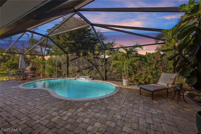 pool at dusk featuring pool water feature, a patio, and glass enclosure