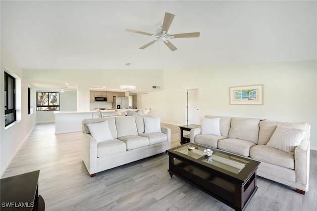 living room with ceiling fan, light hardwood / wood-style floors, and vaulted ceiling