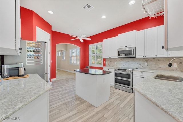 kitchen featuring sink, appliances with stainless steel finishes, white cabinetry, backsplash, and a center island