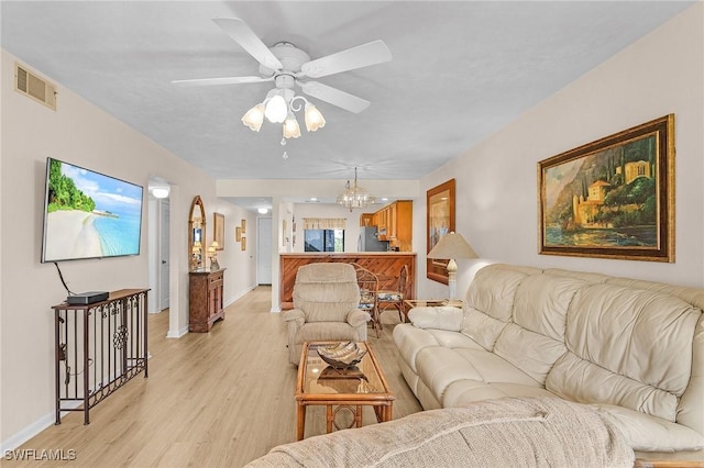 living room with ceiling fan with notable chandelier and light hardwood / wood-style floors