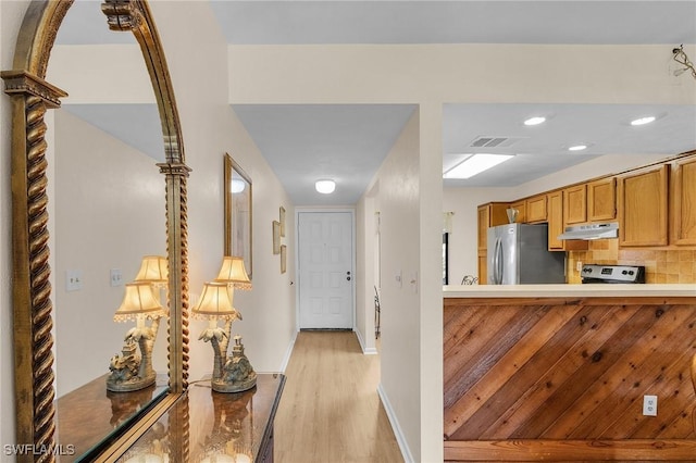 kitchen with decorative columns, appliances with stainless steel finishes, kitchen peninsula, light hardwood / wood-style floors, and backsplash