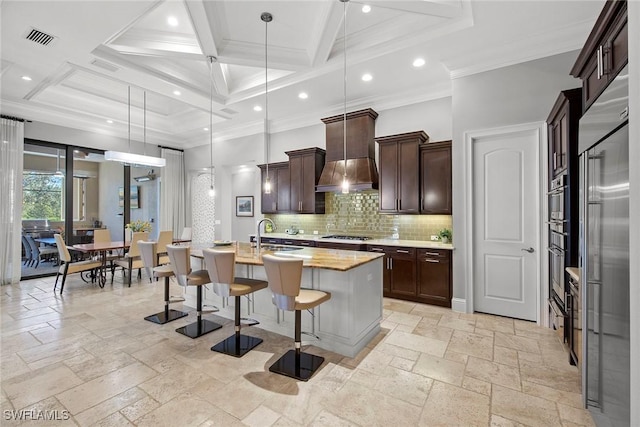 kitchen with a breakfast bar, decorative light fixtures, sink, a kitchen island with sink, and wall chimney range hood