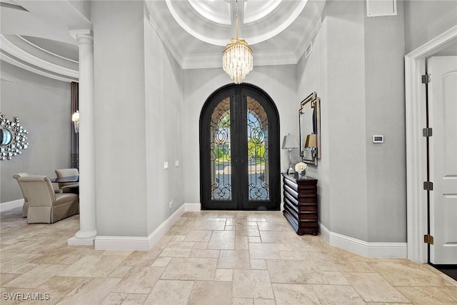 entrance foyer featuring french doors, a chandelier, ornamental molding, a raised ceiling, and decorative columns