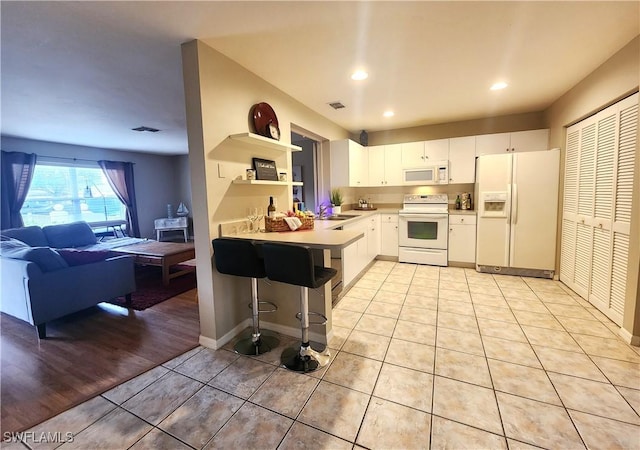 kitchen featuring kitchen peninsula, white cabinetry, light tile patterned floors, white appliances, and a breakfast bar area