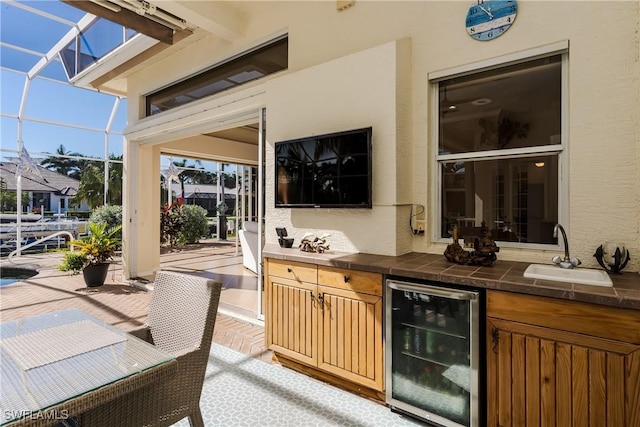 view of patio / terrace featuring glass enclosure, wine cooler, exterior kitchen, and sink