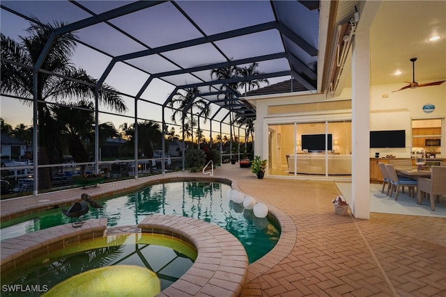 pool at dusk featuring an in ground hot tub, a patio area, and a lanai