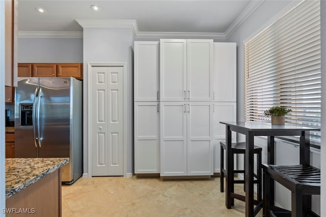 kitchen featuring white cabinets, stainless steel fridge, light stone counters, and crown molding