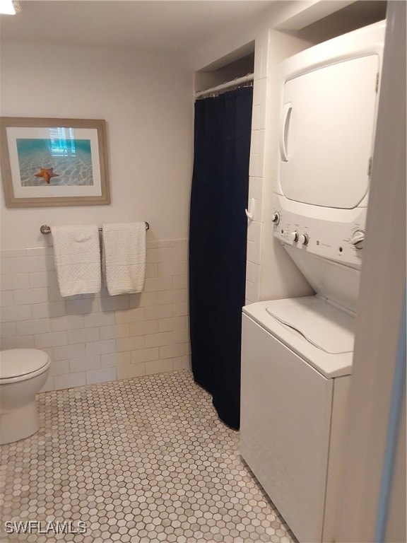 laundry room with tile walls, light tile patterned floors, and stacked washer and clothes dryer