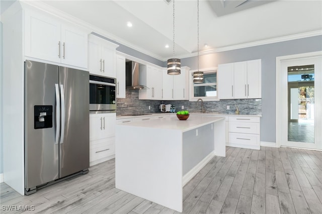 kitchen featuring white cabinets, hanging light fixtures, a kitchen island, wall chimney range hood, and appliances with stainless steel finishes