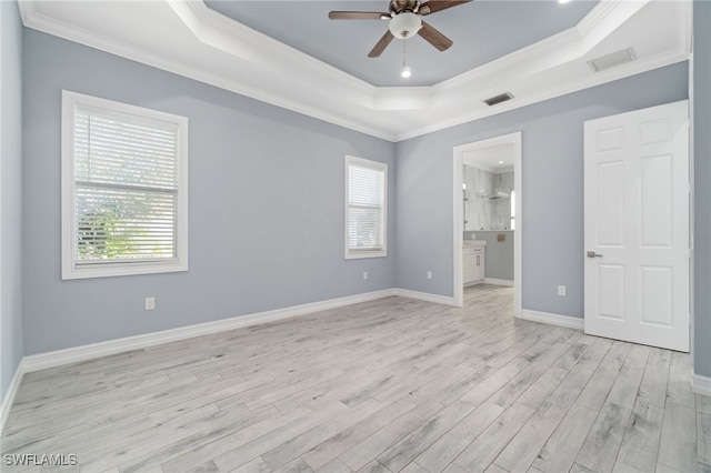 unfurnished bedroom featuring ensuite bathroom, light wood-type flooring, a tray ceiling, crown molding, and ceiling fan