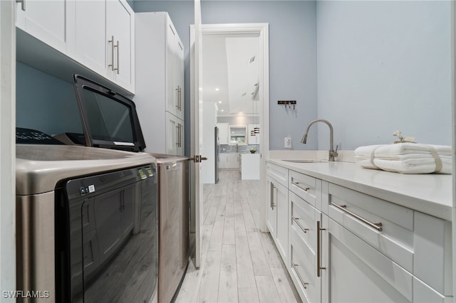 clothes washing area with sink, light hardwood / wood-style floors, cabinets, and separate washer and dryer