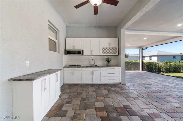 kitchen featuring decorative backsplash, white cabinets, appliances with stainless steel finishes, ceiling fan, and sink