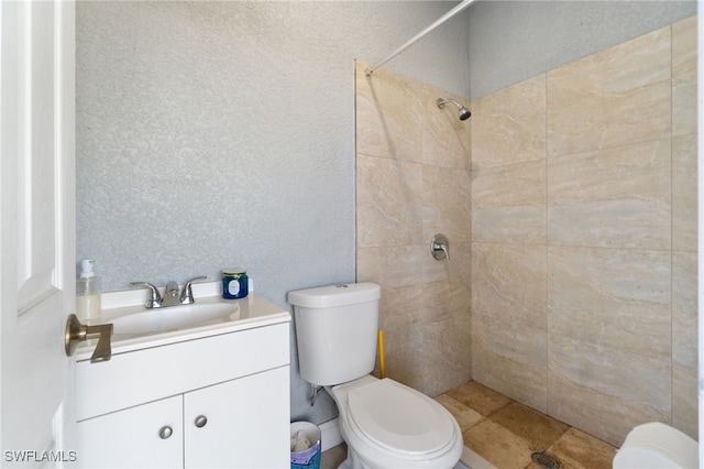 bathroom with toilet, a tile shower, and vanity