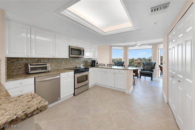 kitchen with white cabinetry, light stone counters, kitchen peninsula, light tile patterned floors, and appliances with stainless steel finishes