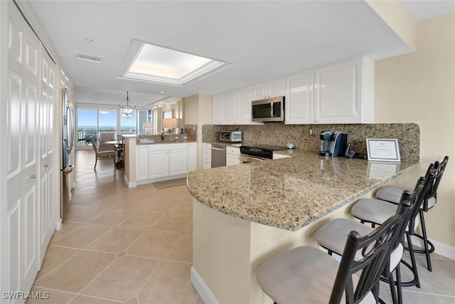 kitchen with kitchen peninsula, a breakfast bar area, light tile patterned floors, white cabinetry, and stainless steel appliances