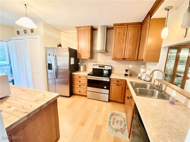 kitchen with sink, pendant lighting, wall chimney range hood, and appliances with stainless steel finishes