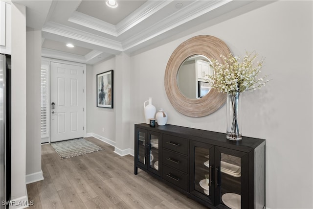 entrance foyer featuring light wood-type flooring, a raised ceiling, and crown molding