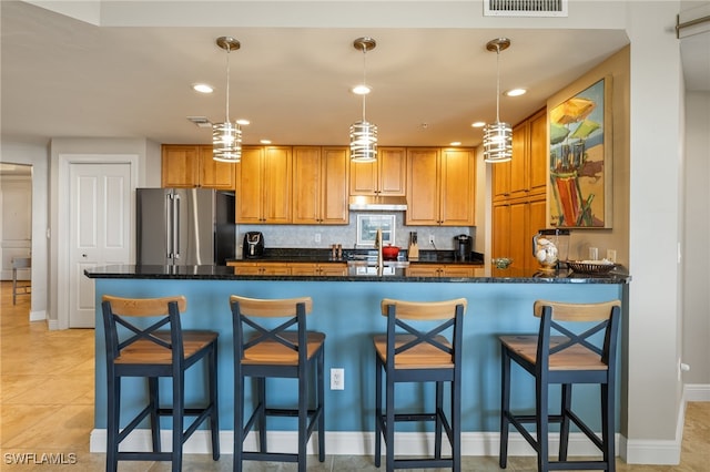 kitchen with stainless steel fridge, a kitchen breakfast bar, dark stone countertops, hanging light fixtures, and light tile patterned flooring