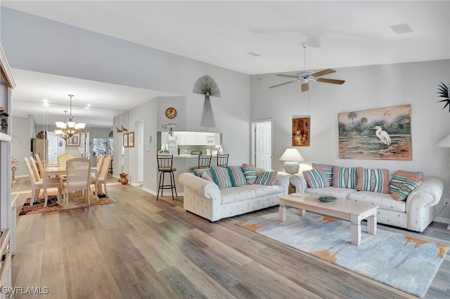 living room with ceiling fan with notable chandelier, vaulted ceiling, and light wood-type flooring