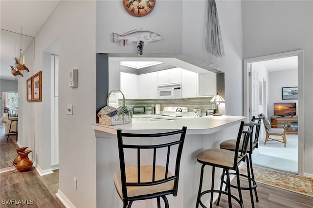 kitchen with white appliances, white cabinets, tasteful backsplash, dark hardwood / wood-style floors, and kitchen peninsula