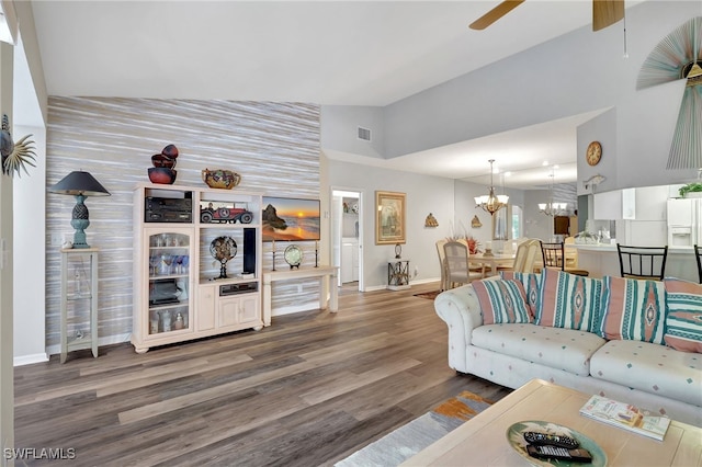 living room with dark wood-type flooring, ceiling fan with notable chandelier, and high vaulted ceiling