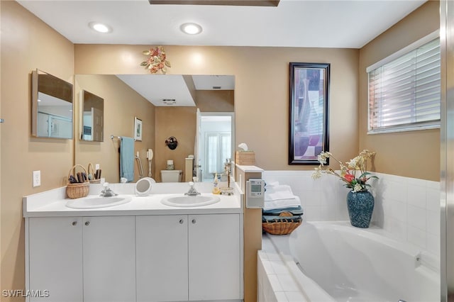 bathroom with toilet, vanity, and tiled tub