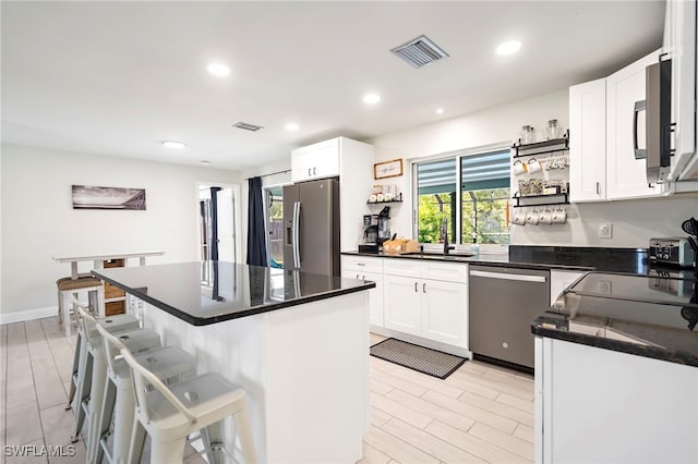 kitchen featuring a breakfast bar, stainless steel appliances, white cabinets, a center island, and light hardwood / wood-style floors