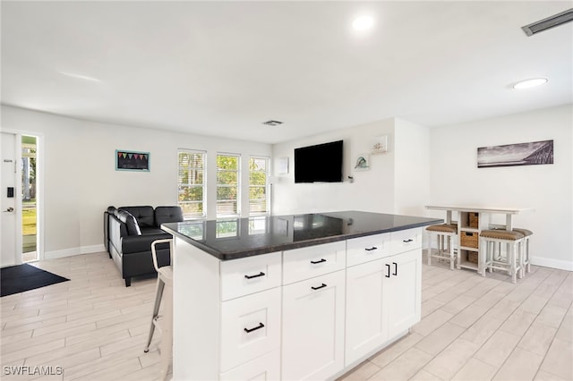 kitchen featuring dark stone counters, a kitchen island, light hardwood / wood-style flooring, white cabinetry, and a breakfast bar area